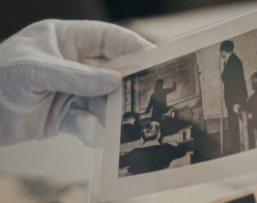 Zbliżenie na dłoń z białej bawełnianej rękawiczce trzymającej czarno-białe zdjęcie przedstawiające lekcję.