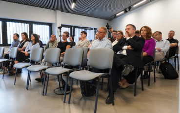 Grupa osób w sali edukacyjnej, w pierwszym rzędzie puste krzesła.