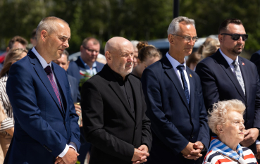 Grupa mężczyzn w średnim wieku w garniturach, przed nimi siedzi starsza kobieta