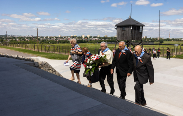 Grupa starszych osób wchodzi po schodach Mauzoleum niosąc w rękach wieniec 
