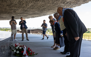 Grupa starszych osób oddaje hołd przed prochami ofiar, bok leży wiązanka z biało-czerwonych kwiatów 