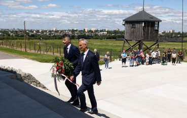 Dwóch mężczyzn w garniturach wchodzi po schodach w rękach trzymając biało-czerwona wiązankę 