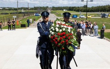 Dwóch mężczyzn w policyjnych mundurach wchodzi po schodach niosąc w rękach wieniec