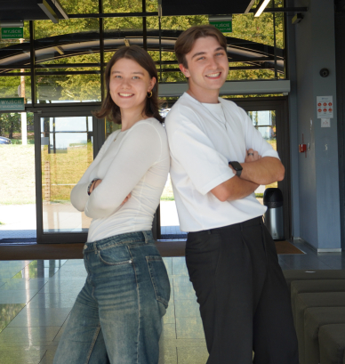 Dwoje młodych uśmiechniętych osób; kobieta i mężczyzna stoją do siebie odwróceni plecami.