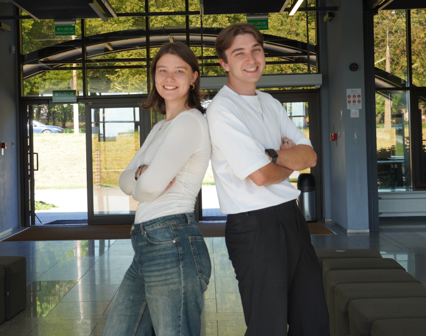 Dwoje młodych uśmiechniętych osób; kobieta i mężczyzna stoją do siebie odwróceni plecami.