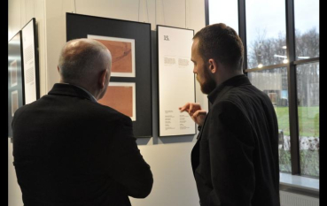 Dwóch mężczyzn ubranych na czarno rozmawia przy panelu wystawy