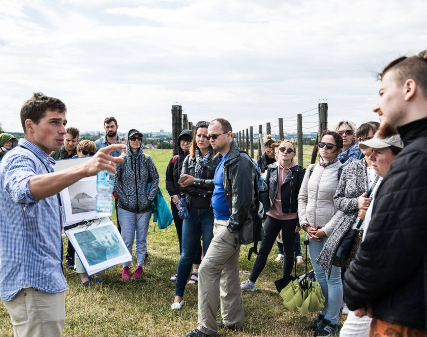 Przewodnik z grupą osób na terenie byłego obozu koncentracyjnego na Majdanku. 