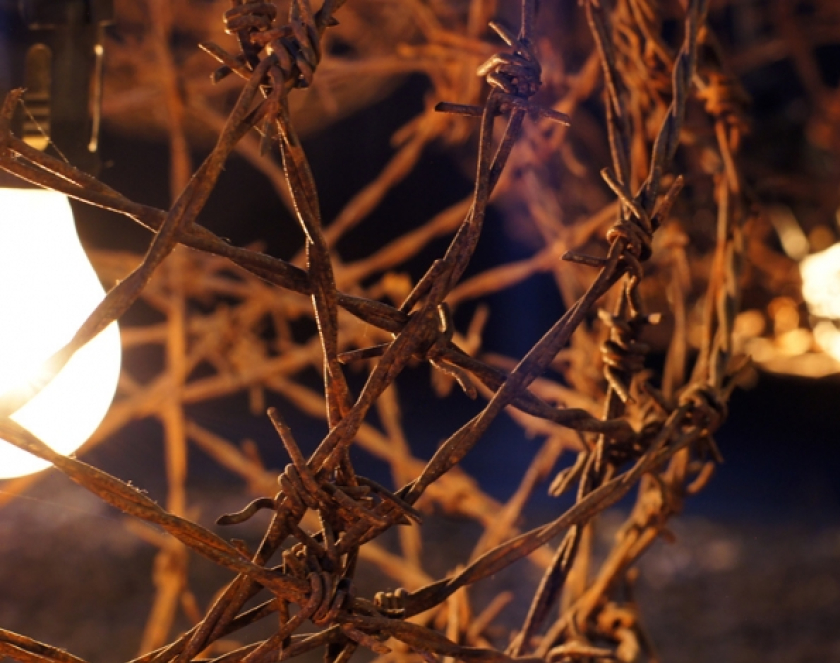 Fragment sfery z drutu kolczastego z żarówką w centrum, dookoła ciemność