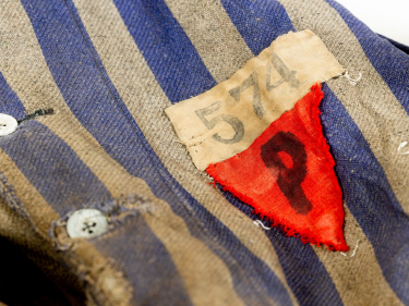 Fragment biało-niebieskiej marynarki w pasy z guzikami. Po prawe stronie naszyty czerwony trójkąt z materiału z literą P. Nad nim prostokątny kawałek tkaniny z numerem 574  
