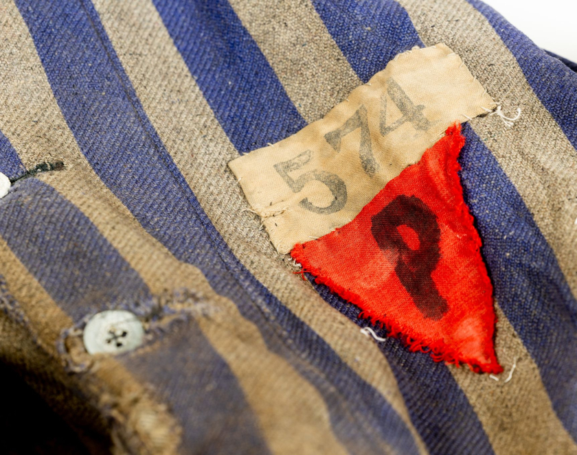 Fragment biało-niebieskiej marynarki w pasy z guzikami. Po prawe stronie naszyty czerwony trójkąt z materiału z literą P. Nad nim prostokątny kawałek tkaniny z numerem 574  