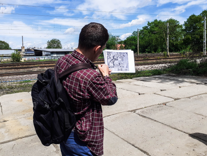 Mężczyzna w koszuli w kratę z plecakiem, trzyma w ręku mapę historyczną. 