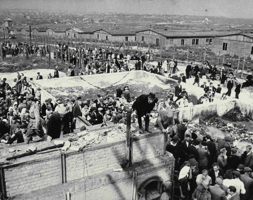 Czarno białe zdjęcie, tłum ludzi na terenie byłego obozu koncentracyjnego na Majdanku; na pierwszym planie starszy mężczyzna stojący na piecu krematoryjnym w pozostałościach po budynku Krematorium.