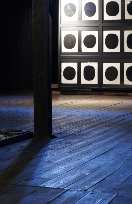 Fragment instalacji artystycznej w drewnianym baraku więźniarskim złożonej z białych prostokątów z czarnym kołem