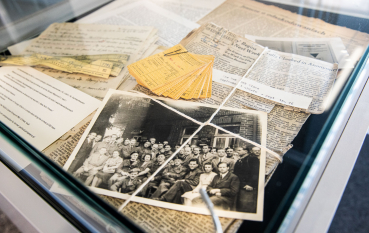 Zdjęcie, fragmenty wycinków z gazet ułożone w szklanej gablocie, widoczny bawełniany biały sznurek