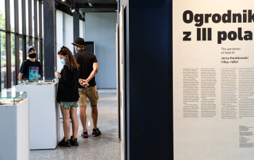 Mężczyzna, kobieta i nastoletni chłopiec na wystawie, na pierwszym planie panel z napisem: Ogrodnik z III pola 