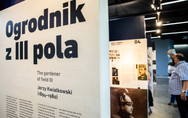 Na pierwszym planie panel wystawy: Ogrodnik z III pola, The gardener of field III Jerzy Kwiatkowski (1894-1980), na drugim planie dwóch mężczyzn 