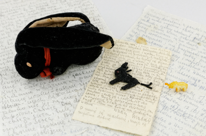 Pluszowa czarna maskotka z długimi uszami, oraz malutka przypominająca konia i mały słonik z kości słoniowej w tle ręcznie pisane listy