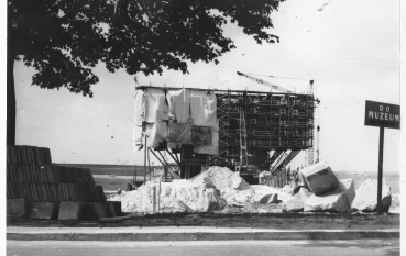 Czarno-białe zdjęcie; Pomnik Brama pokryty rusztowaniem oraz płachtami zabezpieczającymi, przed pomnikiem tabliczka i napis: Do muzeum 