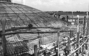 Czarno-białe zdjęcie; fragment kopuły mauzoleum pokryte siecią metalowego zbrojenia, na drugim planie grupa pracowników.