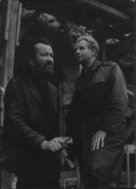 Czarno-białe zdjęcie, dwóch mężczyzn w średnim wieku ubranych na czarno, mężczyzna pierwszy z lewej z ciemną brodą. 