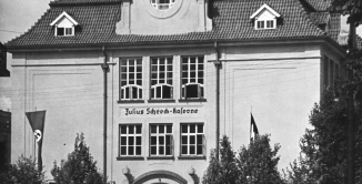 Czarno-białe zdjęcie budynku o charakterystycznym wykuszu; okno w eliptycznej formie zwieńczone półokrągłym daszkiem, wsparte na dwóch cokołach. 