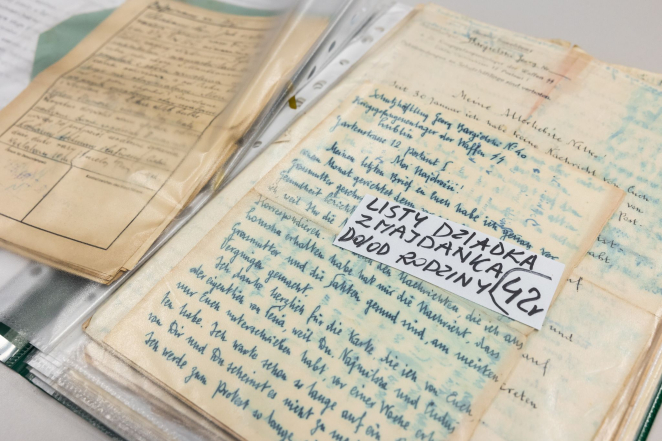 Na zdjęciu dokumenty leżące w dwóch stosach. Na pierwszym leży karta z napisem: listy dziadka z Majdanka do/od rodziny 42 r. 