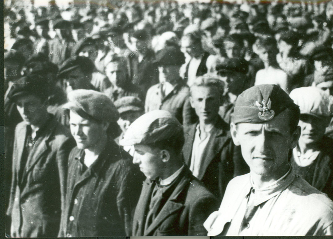 Grupa mężczyzny ubranych w cywilne ubrania, w pierwszym rzędzie mężczyzna z furażerką i orłem