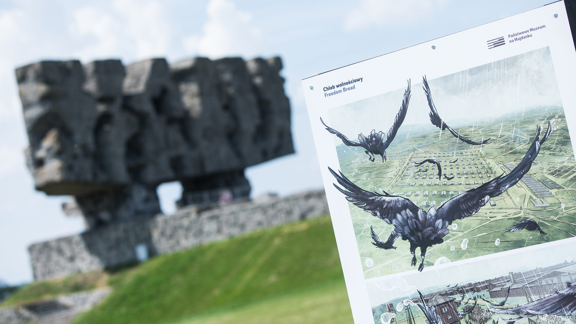 Z lewej strony panel wystawy z rysunkiem ptaków na tle obozu, w tle niewyraźny pomnik-brama na Majdanku