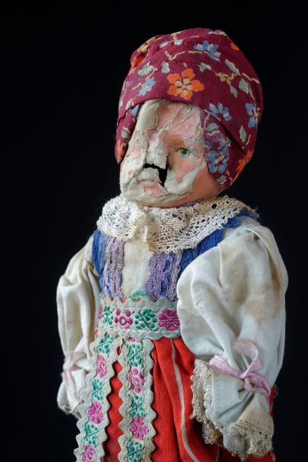 Lalka ze zniszczoną twarzą ubrana w strój ludowy, nakrycie głowy w formie kwiecistej chustki