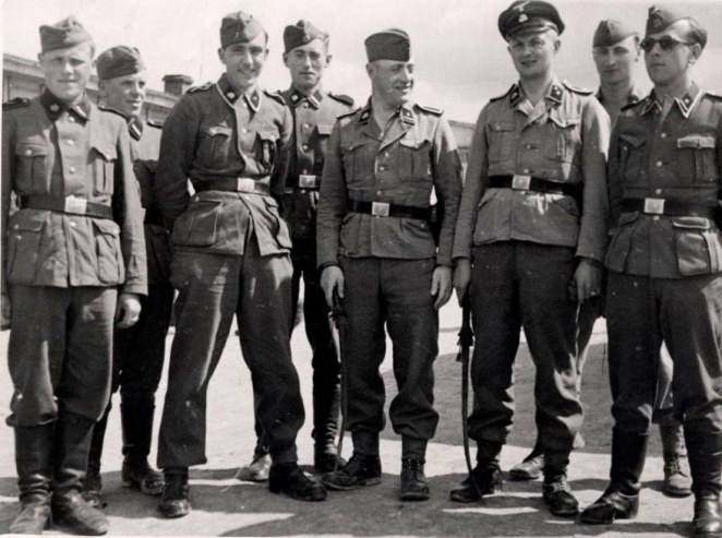 Ośmiu mężczyzn stojących obok siebie ubranych w niemieckie mundury i czapki