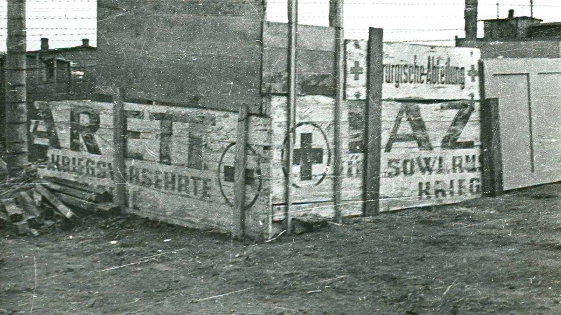 Czarno-białe zdjęcie, ogrodzenie złożone z płyt i napisów w języku niemieckim (LAZ)ARETT i znak krzyża w kole.