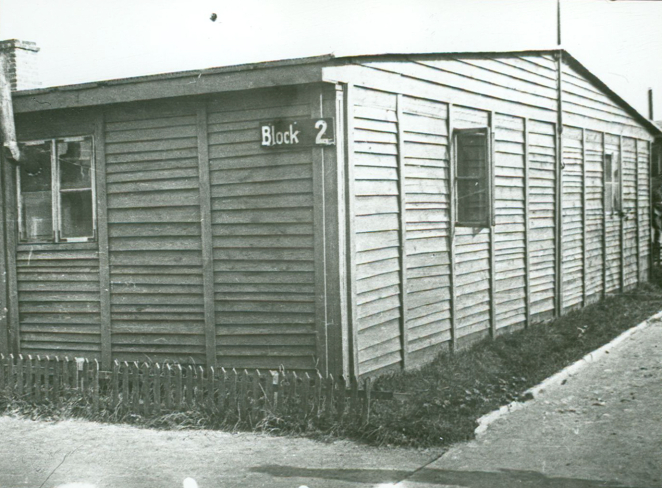 Narożnik baraku z otwartymi oknami. Z przodu tabliczka z napisem w języku niemieckim: Block 2