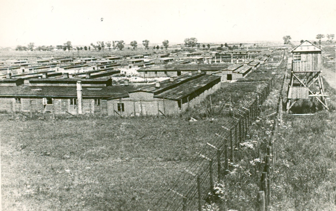 Po lewej stronie zdjęcia baraki, po prawej wieżyczka wartownicza