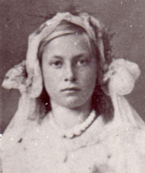 Dziewczynka o jasnych włosach ubrana w strój komunijny. 