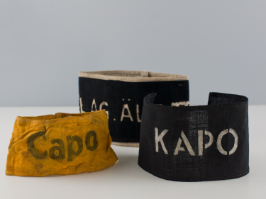 Trzy materiałowe opaski na ramiona z napisami Kapo, Capo i Lag. Alt.