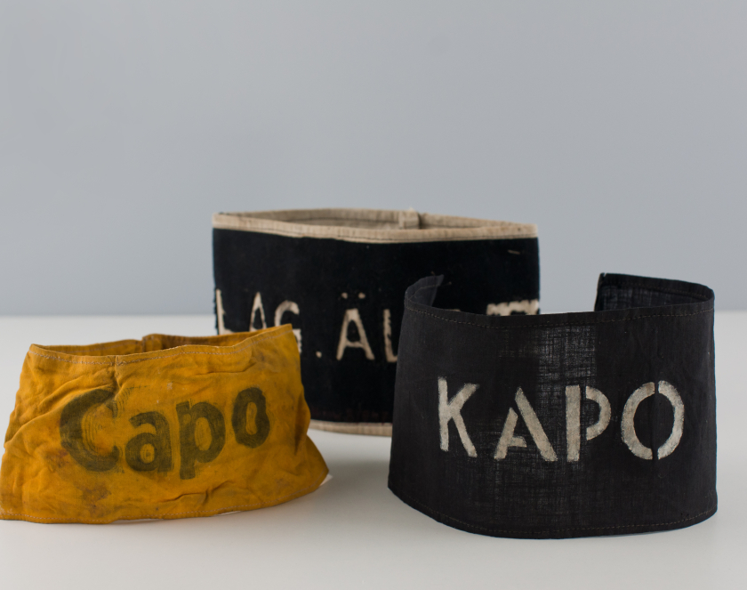 Trzy materiałowe opaski na ramiona z napisami Kapo, Capo i Lag. Alt.