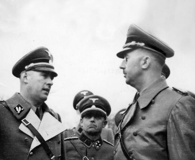 Czarno białe zdjęcie, trzech mężczyzn w niemieckich garniturach, dwóch mężczyzn rozmawia ze sobą, jeden w okrągłych okularach. 