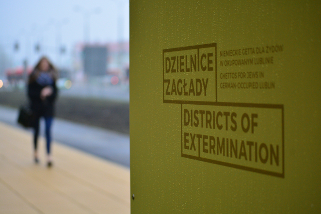Fragment panelu wystawy, napis: Dzielnice Zagłady, Districtis of Extermination, na drugim planie postać kobiety