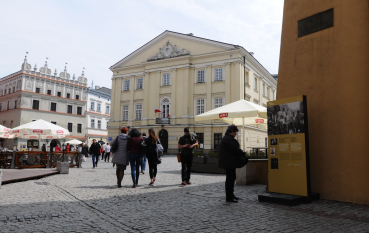 Rynek w Lublinie z Ratuszem Miejskim pośrodku, dookoła grupy ludzi, po prawej stronie panel wystawy