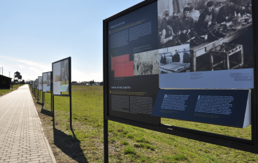 Panele wystawy na terenie Państwowego Muzeum na Majdanku, w tle wieże wartownicze 
