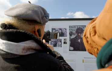 Starsza kobieta robiąca zdjęcie telefonem przy panelu wystawy