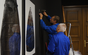 Dwóch mężczyzn ubranych w robocze stroje montuje wystawę 