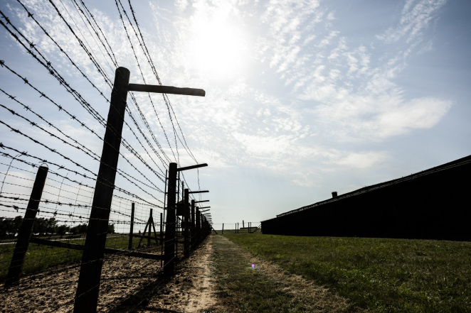 Barak więźniarski i ogrodzenie z drutu kolczastego, słoneczna pogoda.