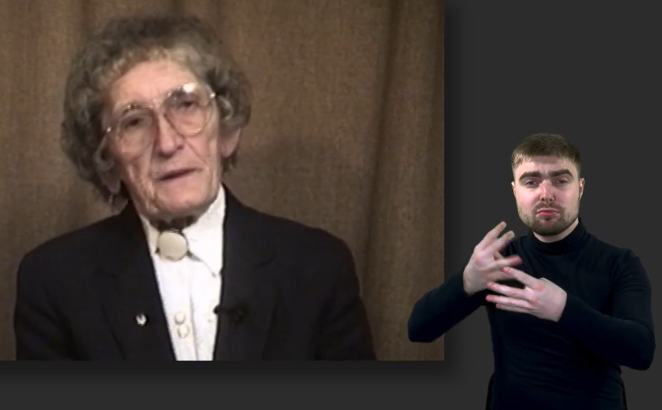 Screen z relacji video, starsza kobieta ubrana w biała koszulę oraz czarną marynarkę, po prawej stronie tłumacz PJM w czarnym golfie 