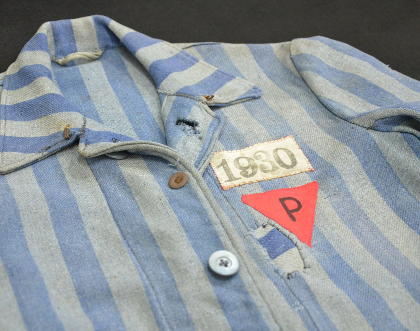 Fragment ubrania więźniarskiego w biało niebieskie pasy, naszyty czerwony trójkąt z literą P, nad nim numer 1930. 