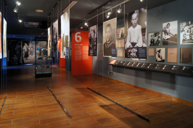 Wnętrze wystawy złożonej z wielkoformatowych zdjęć oraz paneli w kolorze czerwonym z treściami historycznymi
