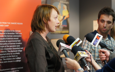 Młoda kobieta o jasnobrązowych włosach udziela wywiadu do kilku mikrofonów