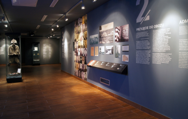 Wnętrze wystawy przeszkolone gabloty z przedmiotami, w tle historyczne zdjęcia oraz portrety 