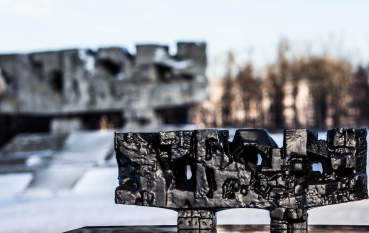 Na pierwszym planie model 3d Pomnika-Bramy wykonany z czarnego materiału, na drugim planie zarys Pomnika-Bramy (abstrakcyjnej kamiennej formy).