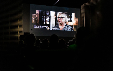 50-letnia kobieta z jasnymi włosami do brody na tle baraku więźniarskiego. 